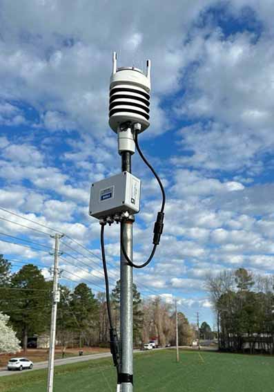 An Orion Weather Station installed at a Johnston County 911 site. Behind it is a blue, partly-cloudy sky.